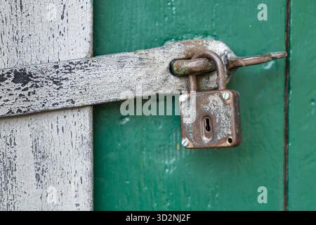 Old rusted padlock securing a wooden door with peeling green and white paint, Zellerndorf Stock Photo