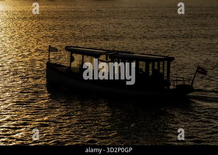 Small boat sailing on Daugava River in Riga under golden sunset light creating calm water reflections, peaceful Baltic atmosphere, and evening silhoue Stock Photo