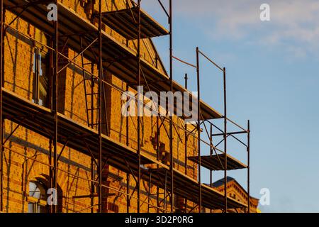 Metal scaffolding system attached to old brick facade during restoration project in Riga illustrating structural reinforcement, architectural stabiliz Stock Photo