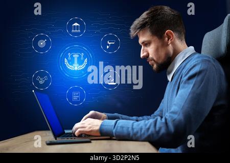 Professional man working on laptop with digital icons representing law and technology concepts Stock Photo