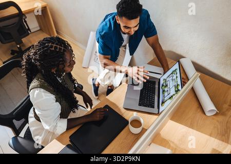 Two young professionals working together on a laptop, discussing architectural designs in a modern, collaborative workspace. Stock Photo