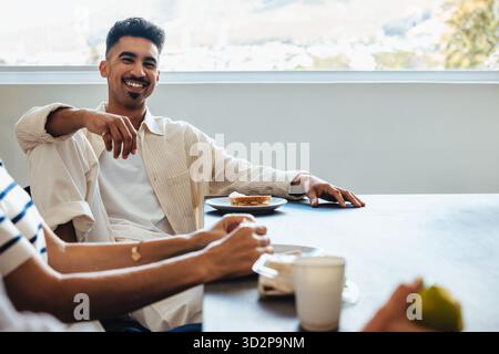 A cheerful young man having an engaging conversation with colleagues during a break at work. The modern office environment enhances the connection and Stock Photo
