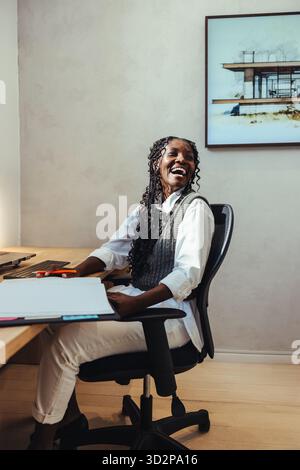 A female architect in her 30s smiles while working at her desk. The office setting emphasizes professionalism and modernity, complemented by architect Stock Photo