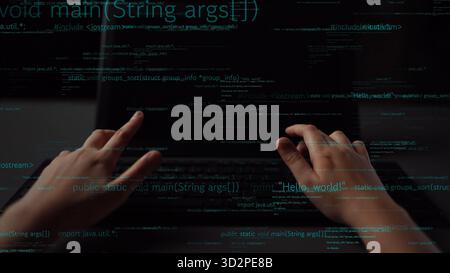 Hands are seen typing on a laptop in a dark environment, with lines of code displayed on the screen. This image captures the essence of programming an Stock Photo