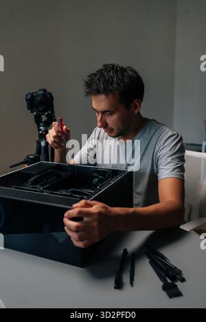 Vertical portrait of computer technician disassembling desktop pc, wielding precision screwdriver while recording tutorial video on tripod-mounted Stock Photo