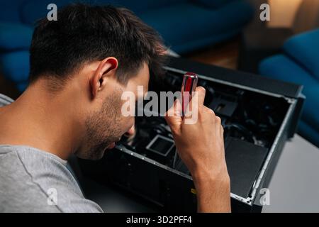 Top view from shoulder of skilled technician disassembling desktop computer using precision screwdriver while performing intricate hardware diagnostic Stock Photo