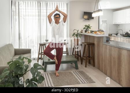Man balancing in tree pose, practicing wellness and mindful living in his home living room Stock Photo