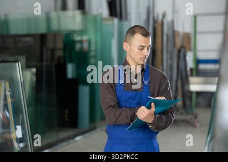 Worker inspecting glass panels and recording check results Stock Photo