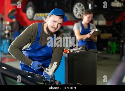 Professional mechanic man in uniform repairing car in auto repair garage Stock Photo
