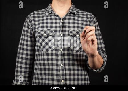 Close up to a young man writing with his left hand in the space in front of him and a black background Stock Photo