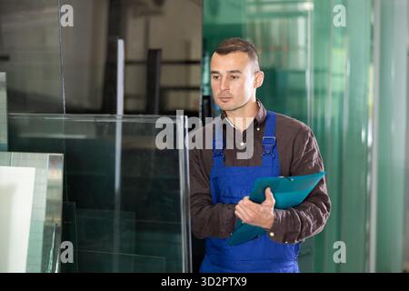 Worker inspecting glass panels and recording check results Stock Photo
