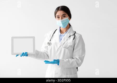Young Hindu Lady Doctor in Protective Gear Using Tablet to Communicate Safely During Pandemic Stock Photo