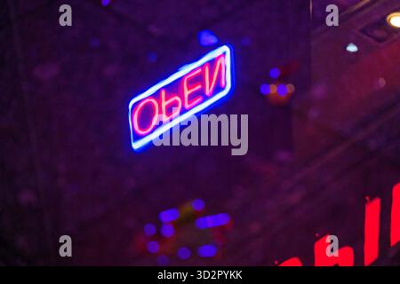 Closeup of a bright neon OPEN sign in red and blue colors, reflected in a window. Urban nightlife concept, modern design, and vibrant city aesthetic w Stock Photo