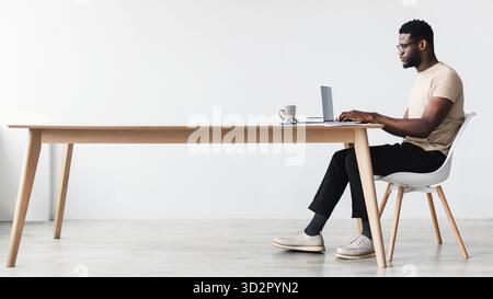 Focused Young Black Man Working on Laptop at Home Office Desk Stock Photo