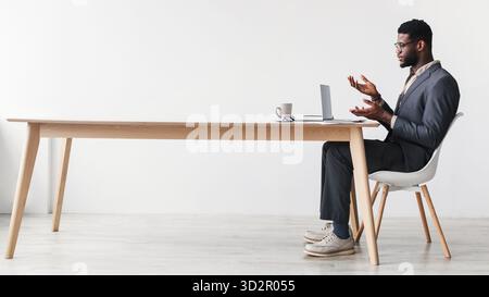 Black Man in Formal Wear Engages in Web Conference From Desk Setup in Home Office Stock Photo