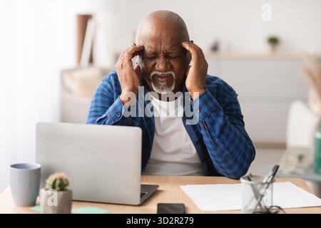 Senior Black Businessman Experiencing Headache While Working at Desk in Modern Office Stock Photo