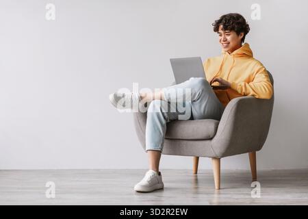 Young Asian Man Enjoys Remote Work While Sitting Comfortably in an Armchair Stock Photo