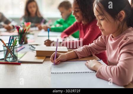 Korean Schoolgirl Taking Notes While Learning With Classmates in Modern Classroom Setting Stock Photo