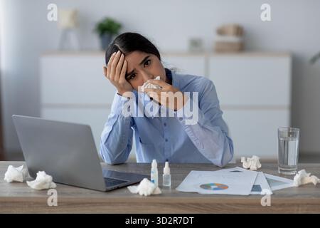 Unhappy Young Indian Woman Feeling Ill at Her Office Desk While Managing Workplace Tasks Stock Photo