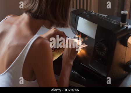 Close-up detail of a woman, while sewing satin fabric on a sewing machine. Over the shoulder scene of step by step in the sewing process, handmade. Stock Photo