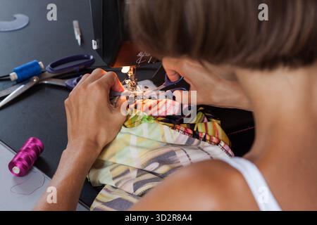 Close-up detail of a woman’s hands trimming the thread with small scissors, while working on a sewing machine. Step by step in the sewing process. Stock Photo