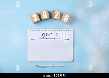 New 2026 Year Goals. Inscription in notebook and cubes with numbers on light blue background, top view. Bokeh lights Stock Photo