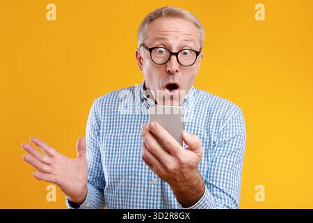 Mature Man Celebrates Exciting News Using Smartphone Against Bright Background Stock Photo
