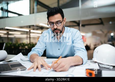 Engineer Working on Detailed Plans in a Modern Office Setting During the Day Stock Photo
