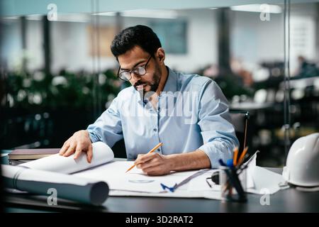 Young Professional Works on Architectural Plans at a Modern Office During the Day Stock Photo