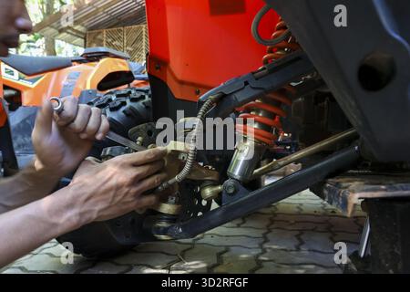Focused mechanic man with wrench in hand performs repair and maintenance, fixing suspension on an all terrain vehicle. This work requires concentratio Stock Photo