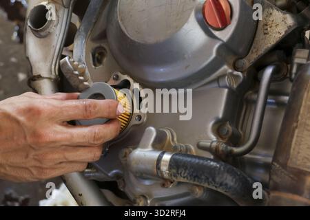 Concentrated mechanic hand performing repair and maintenance on motorcycle engine. Professional service in garage changing oil filter for motor vehicl Stock Photo