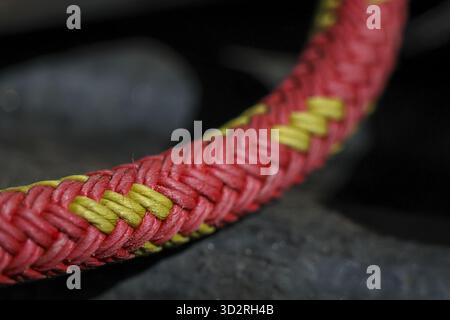 Detailed macro close up of strong red and yellow braided rope showing its woven fiber texture and pattern. focus highlights material and craftsmanship Stock Photo