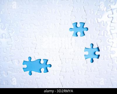 Concept of incompleteness and missing parts with three empty spaces in white jigsaw puzzle on blue background. Represents gap, imperfection, missing e Stock Photo