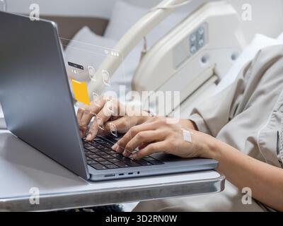 Remote work concept showing a hospitalized person typing on a laptop with virtual file transfer interface. Illustrates productivity, digital workflow, Stock Photo