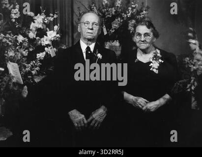 Married couple grimily sit for their 50th anniversary portrait, c. 1950. Stock Photo