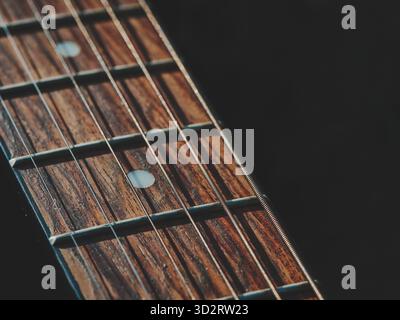 Guitar neck close up, angled from right to left, sharp focus on frets and wood texture, left side dark empty space for text, warm subtle tones, minima Stock Photo