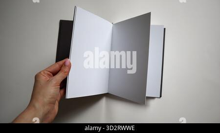 Woman's hand holds an open notebook with blank white pages on a light background. Concept of idea, learning, business, a new project. Image is suitabl Stock Photo