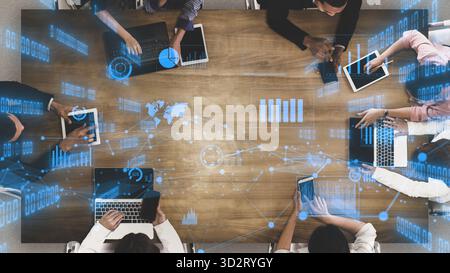 A dynamic business meeting scene showcasing professionals engaged with laptops and tablets, featuring digital analytics and charts to enhance collabor Stock Photo