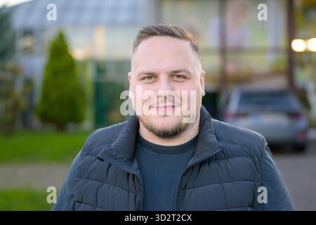 Relaxed young man with short hair and beard smiling confidently outdoors in soft evening light. Stock Photo