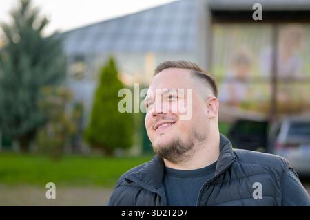 Smiling young man with short hair and beard looking away outdoors in soft natural daylight. Stock Photo