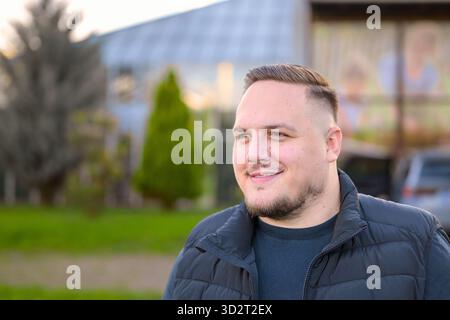 Cheerful young man with short hair and beard smiling confidently outdoors in natural sunlight. Stock Photo