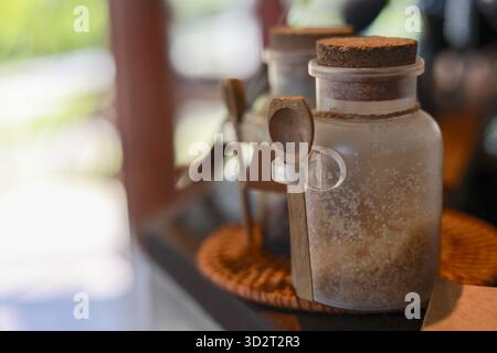 Rustic close up of glass seasoning jar with cork stopper and wooden scoop, on coaster, creates warm and cozy atmosphere in cafe or kitchen setting Stock Photo