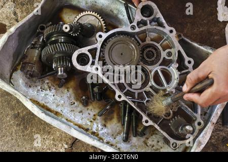Meticulous mechanic cleaning dirty transmission gearbox case with brush. Close up view of human hand working on oily metal engine part during auto rep Stock Photo