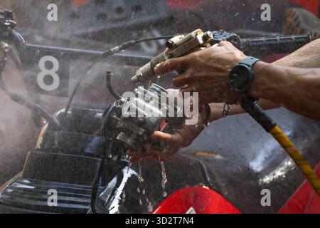 Focused mechanic hand washing race car engine with water spray. This detailed motor maintenance shows precision and preparation before competition Stock Photo