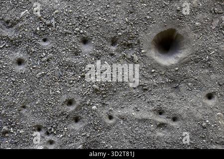 Gray abstract background of textured sand ground surface with many small holes and pits. close up view showing detail of rough, dry soil, creating mys Stock Photo