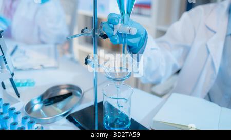 Two female scientists in white lab coats working together in a bright laboratory with microscopes, glassware, and blue test tubes, representing teamwo Stock Photo