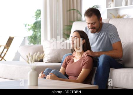 Man massaging his partner sitting on a couch at home Stock Photo
