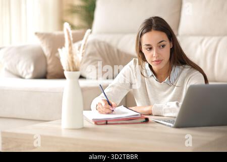 Student taking notes watching online course on laptop at home Stock Photo