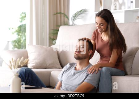 Woman massaging her partner sitting on a couch at home Stock Photo