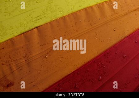Colorful umbrella fabric with vibrant yellow, orange, and red stripes appears wet with numerous small water droplets. abstract close up creates refres Stock Photo
